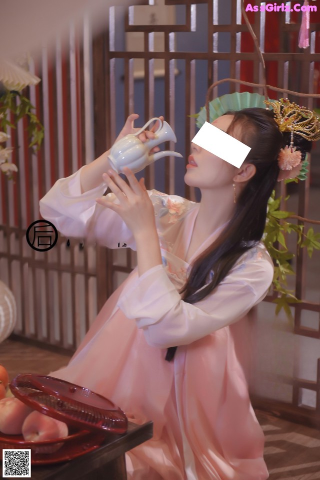 A woman in a pink dress holding a teapot in her hand.