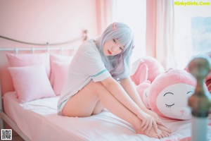 A woman in a pink lingerie sitting on a bed with stuffed animals.