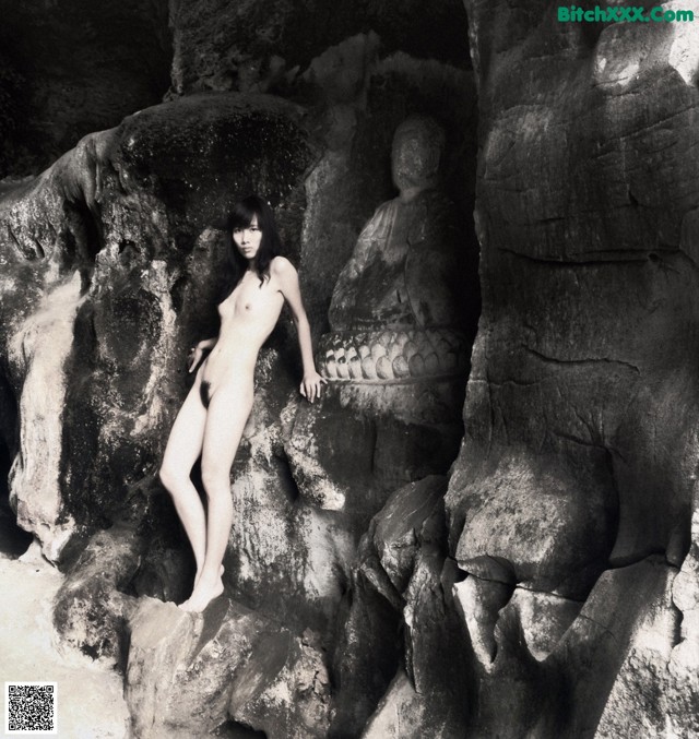 A naked woman standing in front of a rock formation.
