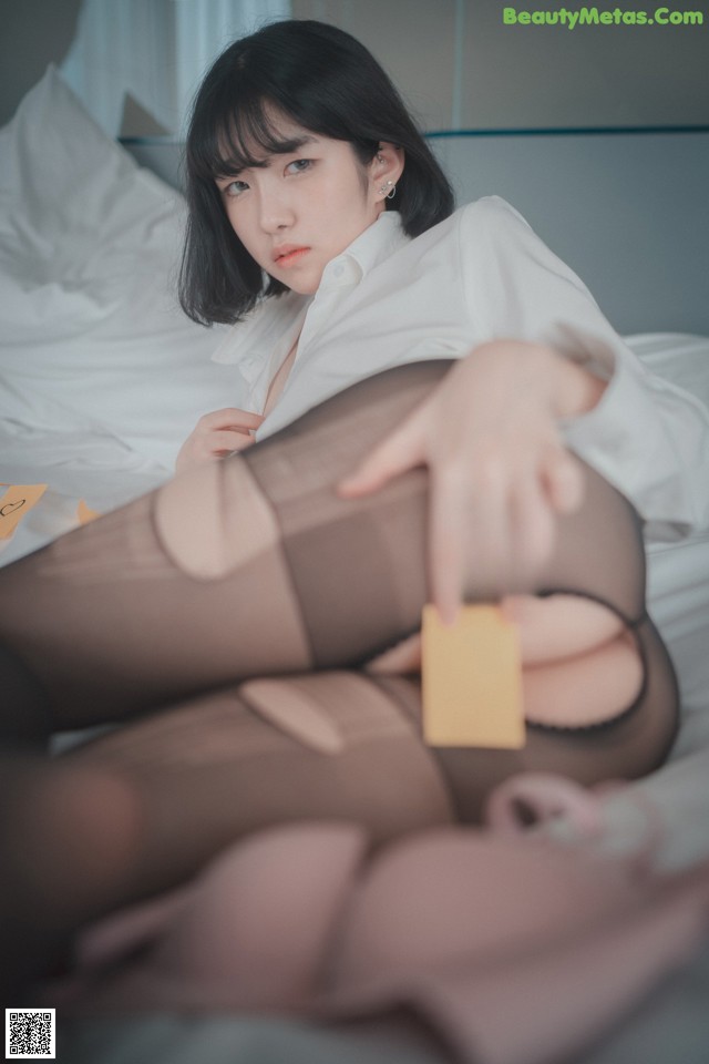 A woman in a white shirt and black stockings laying on a bed.