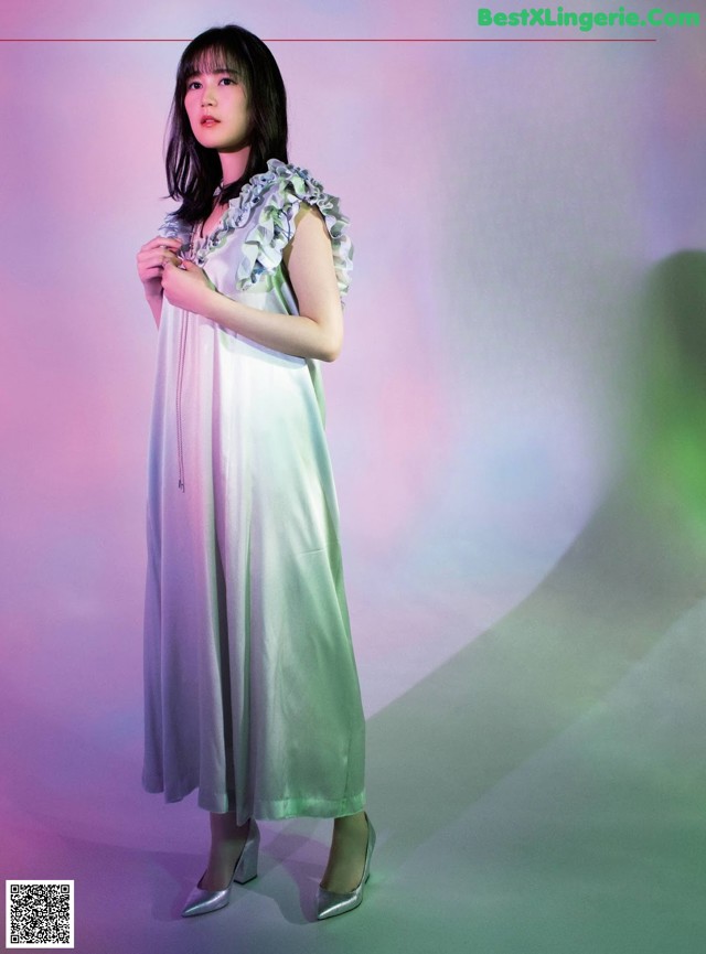 A woman in a white dress standing in front of a pink and green background.