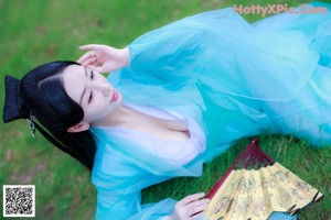 A woman in a blue dress sitting on a bed.