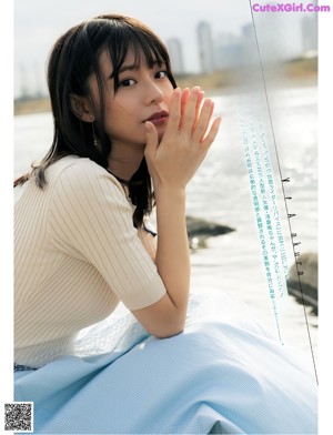 A woman in a white top and blue skirt posing by the water.