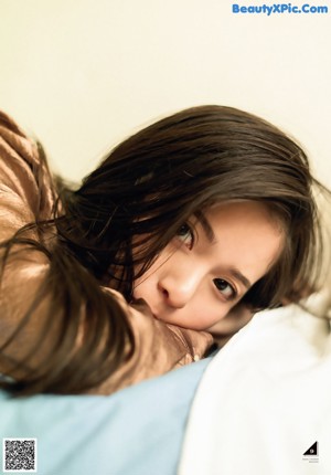 A woman in a blue shirt with her hand on her chin.