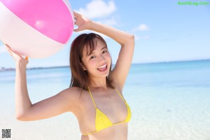 A woman in a yellow bikini holding a beach ball.