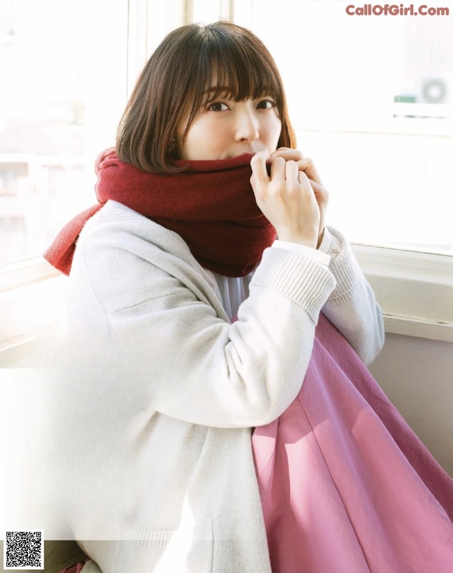 A woman sitting on a window sill wearing a scarf.