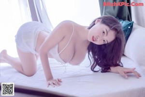 A woman in a white lingerie sitting on a bed.