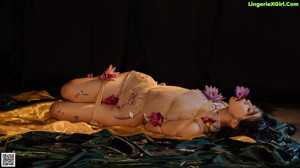 A woman in lingerie sitting on a bed next to a plant.