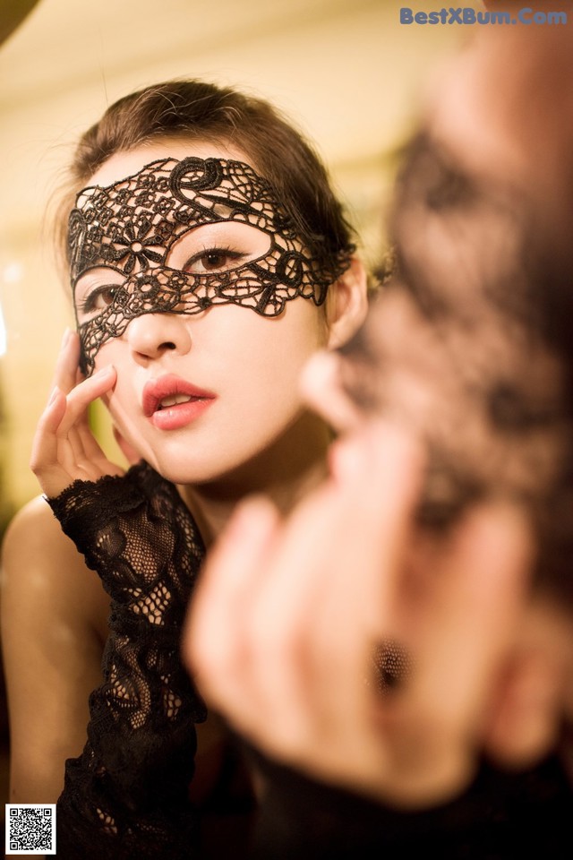 A woman wearing a black lace mask in front of a mirror.