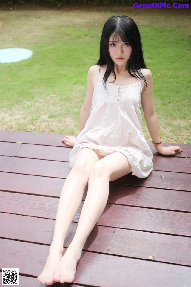 A woman sitting on a wooden deck in a white dress.