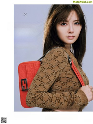 A woman in a black suit holding a red handbag.