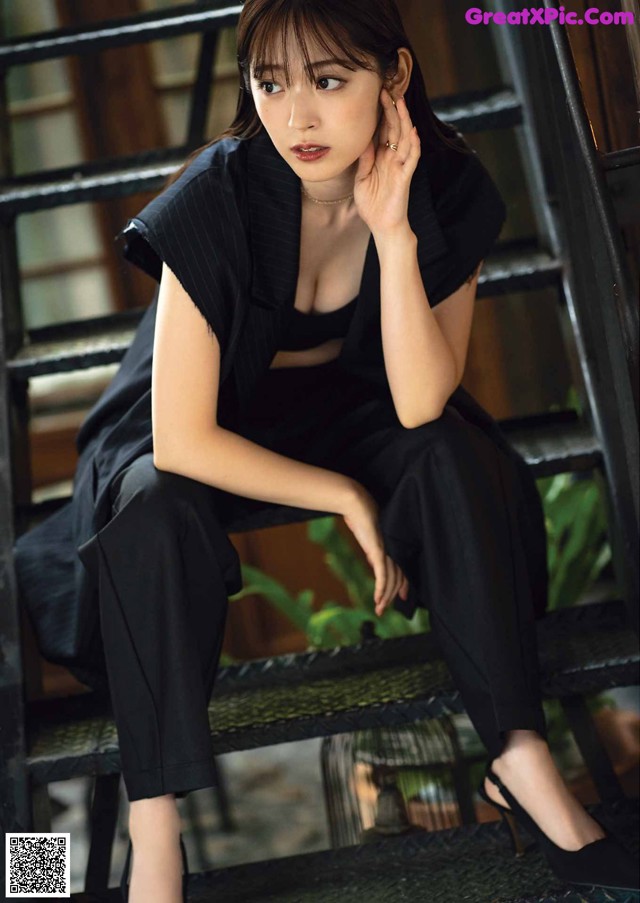 A woman sitting on a set of stairs wearing a black suit.