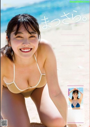 A woman in a bikini standing on a beach next to a drink.