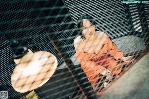 A woman in an orange jumpsuit leaning against a window.