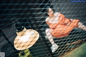 A woman in an orange jumpsuit sitting on the floor next to a toolbox.