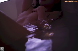 A naked woman standing in a bathtub next to a window.