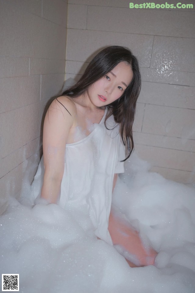 A woman sitting in a bathtub filled with foam.