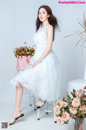 A woman in a white dress sitting on a wooden bench.