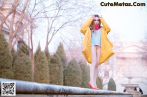 A woman in a blue sweater and red high heels leaning against a wall.