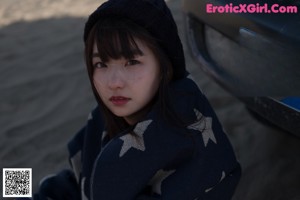 A woman sitting on a sand dune wrapped in a blanket.