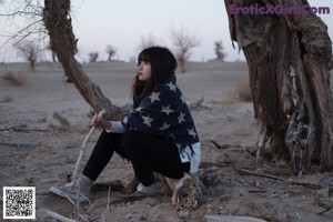 A woman sitting on the ground next to a car.