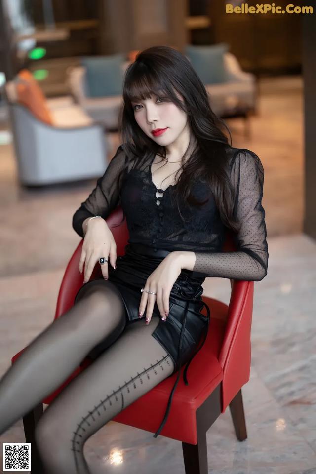 A woman sitting on a red chair in a black dress.