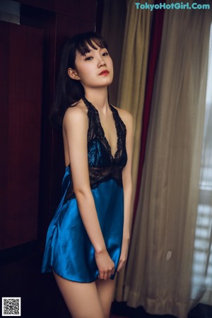 A woman in a blue dress posing in front of a window.