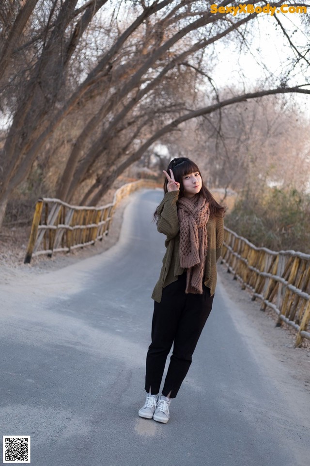 A woman standing on the side of a road with trees in the background.