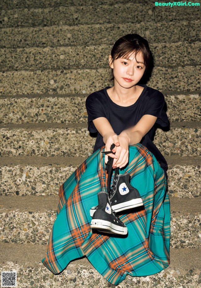 A young woman sitting on the steps of a building holding a pair of shoes.