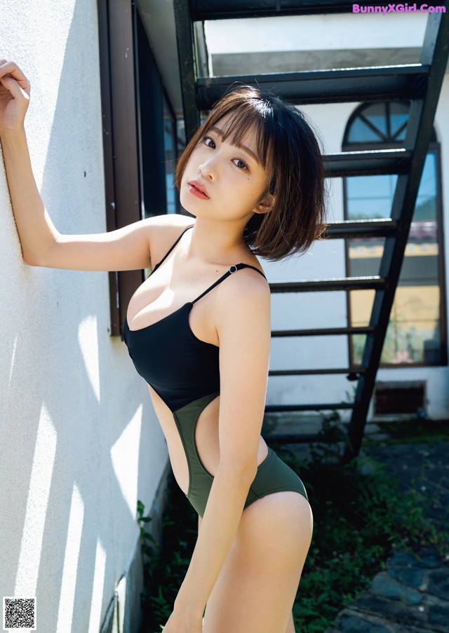 A woman in a black and green bathing suit leaning against a wall.