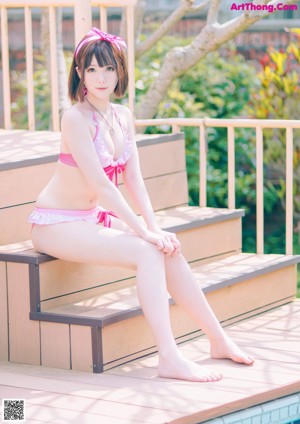A woman in a pink bikini sitting on a wooden deck.