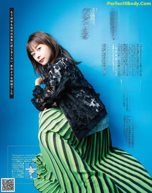 A woman in a black top and green skirt posing for a magazine.