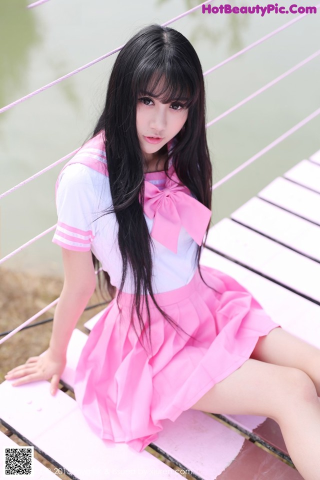 A woman in a pink dress sitting on a wooden bridge.