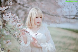 A woman in a white dress sitting under a tree.