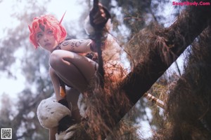 A woman with red hair holding a sword in the woods.