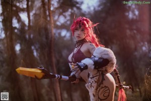 A woman with red hair holding a sword in a forest.