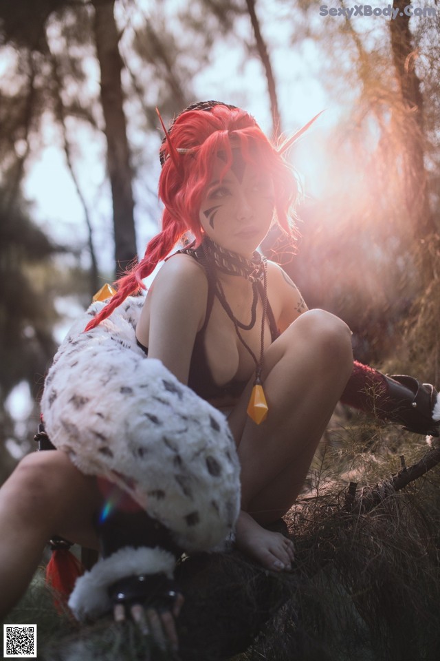 A woman with red hair sitting on a rock in the woods.