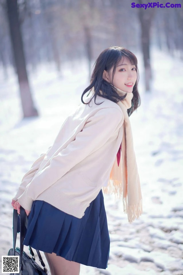 A woman in a white sweater and blue skirt holding a black bag.