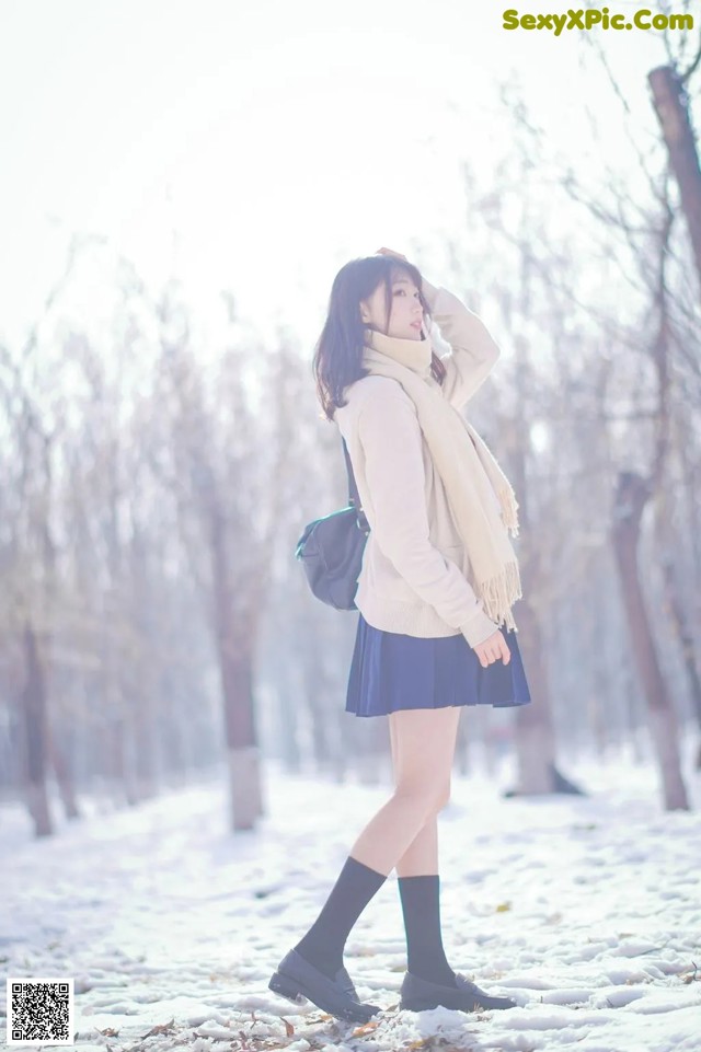 A woman in a white sweater and blue skirt standing in the snow.