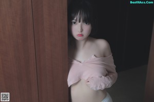 A woman in a pink shirt and white panties leaning against a window.