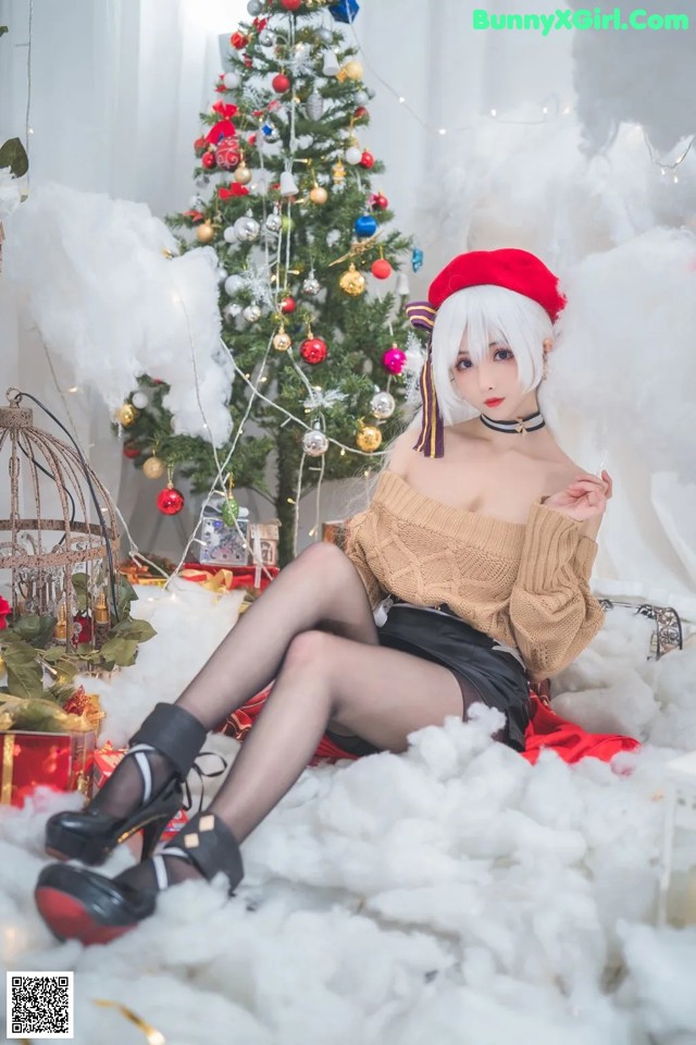 A woman sitting on a bed in front of a Christmas tree.