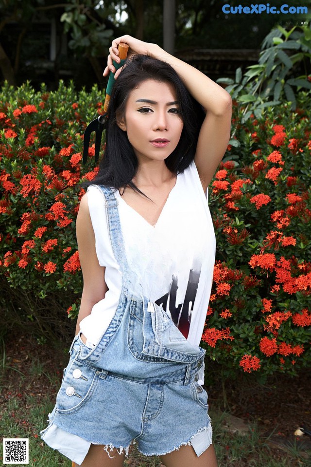 A woman in a white tank top and denim overalls posing for a picture.