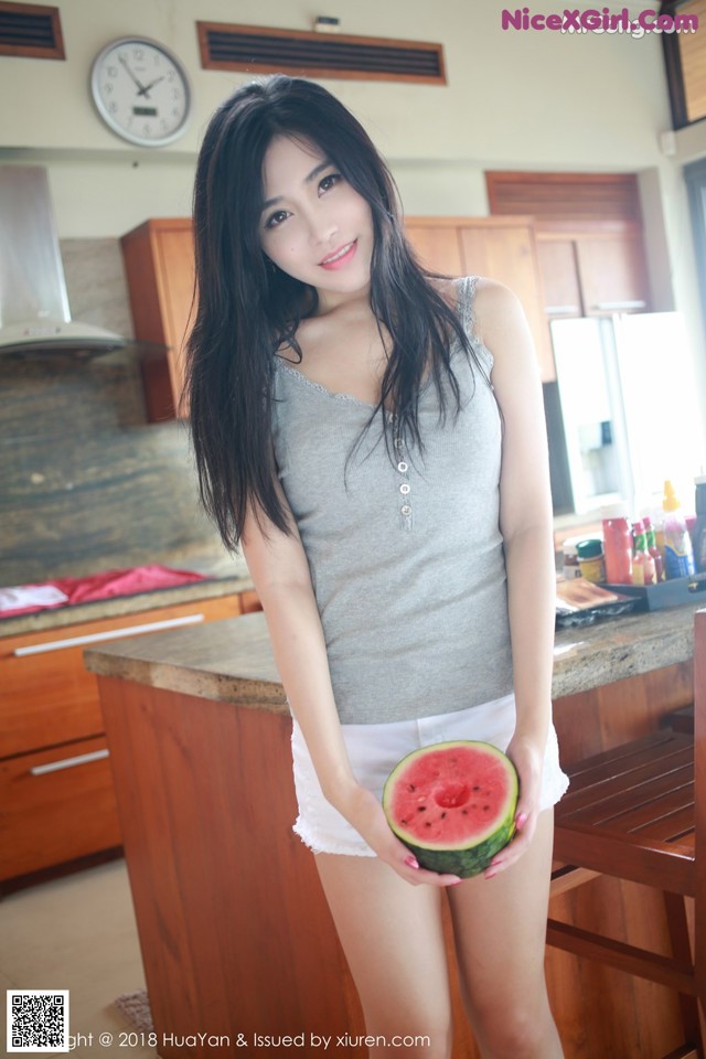 A woman holding a slice of watermelon in a kitchen.