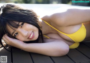 A woman in a yellow bikini laying on a wooden deck next to a pool.