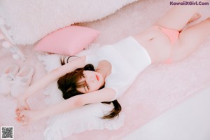 A woman in a white shirt and pink panties laying on a white rug.