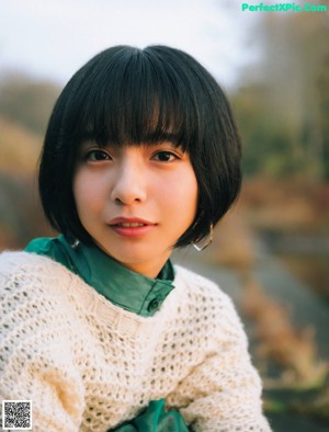 A woman sitting on a couch wearing a white sweater with red roses on it.