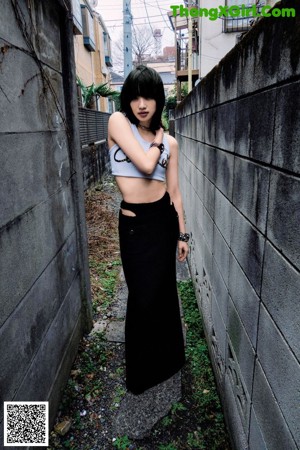 A woman leaning against a wall wearing a white top and black shorts.