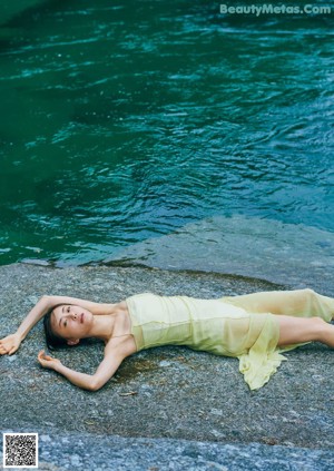 A woman in a yellow dress sitting on a rock by a stream.