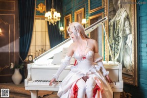 A woman in a white and pink dress sitting on a white piano.